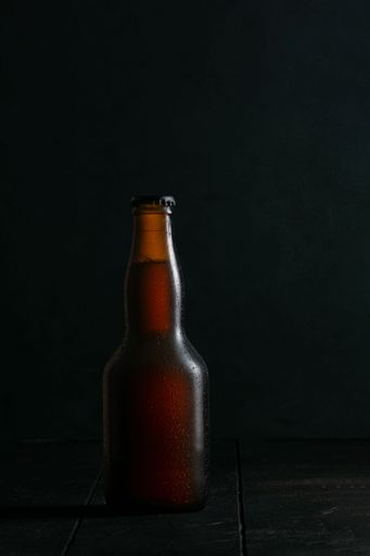A vertical closeup shot of a brown glass beer bottle on a wooden table with a black background