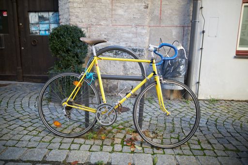 A side view of yellow bicycle locked onto a metal structure on cobblestone sidewalk