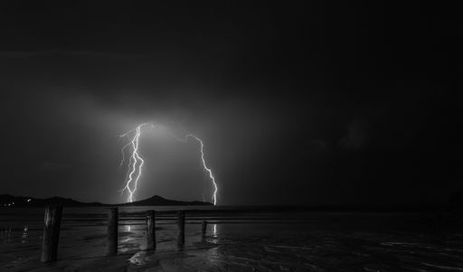 A stunning grayscale shot of a distant lightning strike from a pier
