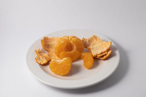 A closeup shot of a tangerine surrounded by peels on a white plate
