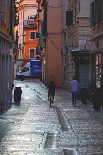 A back view of two people walking and cycling on narrow street in the morning in Verona