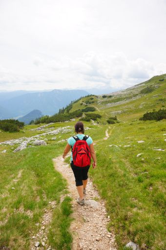 Woman with red backpack walking on a footpath in the Alp mountains.