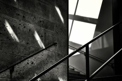 A grayscale shot of the railing of a staircase next to a stone wall - unknown future concept