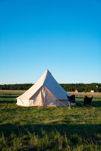 A vertical shot of a tent and lawn chairs on a grassy landscape on a sunny day.