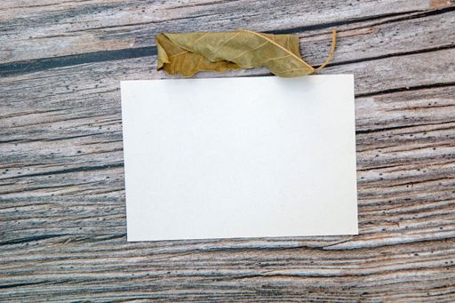 A top view of a blank sheet of paper with copy space and a dried leaf on a wooden surface