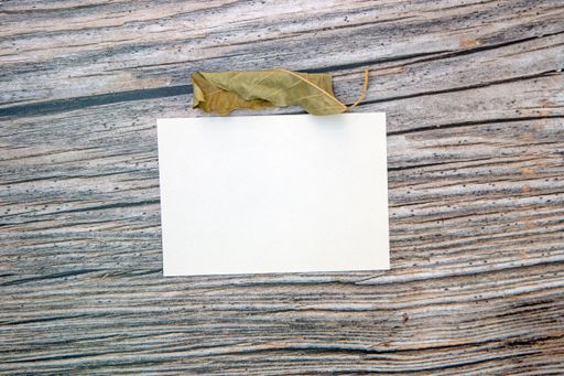 A top view of a blank sheet of paper with copy space and a dried leaf on a wooden surface
