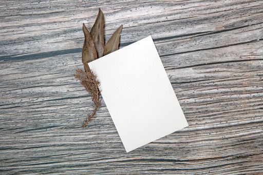 A top view of a blank sheet of paper with copy space and dried leaves on a wooden surface