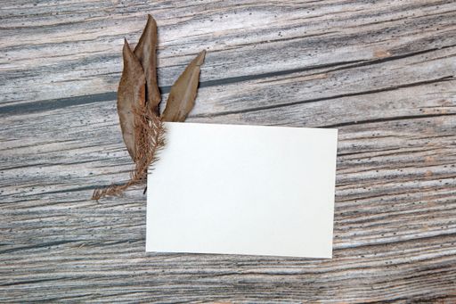 A top view of a blank sheet of paper with copy space and dried leaves on a wooden surface