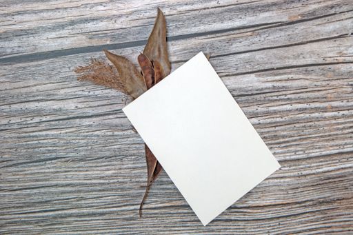 A top view of a blank sheet of paper with copy space and dried leaves on a wooden surface
