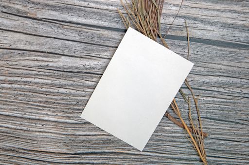 A top view of a blank sheet of paper with copy space and dried plants on a wooden surface