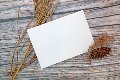A top view of a blank sheet of paper with copy space and dried plants on a wooden surface