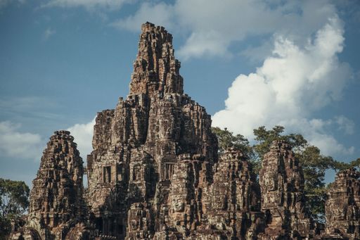 An aerial view of Angkor Wat temple surrounded by growing trees under blue bright sky