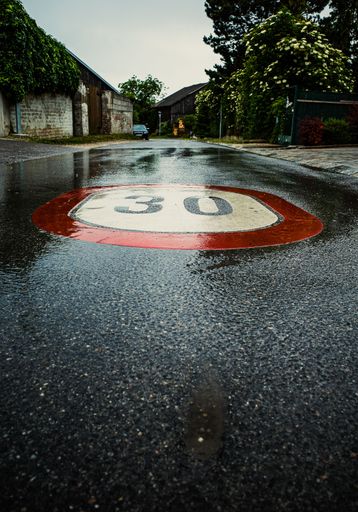 A vertical shot of a large sign painted on the rain-wetted ground marking the allowed speed limit