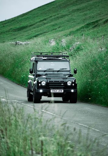 A vertical shot of a Land Rover driving on a mountain road on a cloudy day