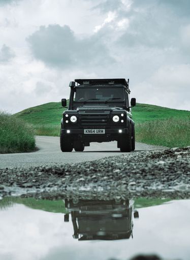 A vertical shot of a Land Rover driving on a mountain road on a cloudy day