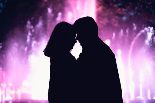 A silhouette of a romantic couple standing together holding each other on blurred purple background