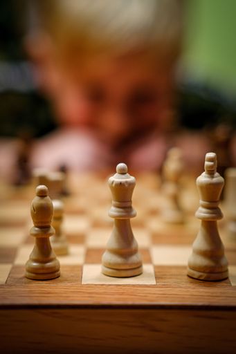 A vertical shot of a child playing chess and the focus on the pieces