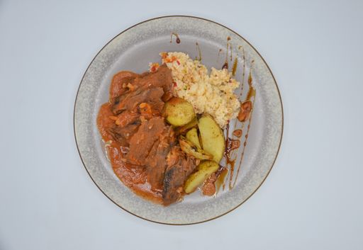 A closeup shot of pork with sauce with rice and potatoes