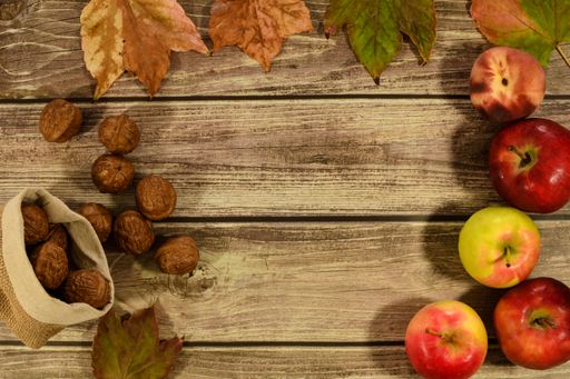 Autumn leaves, apples, a peach and nuts on a wooden table with a space for a text