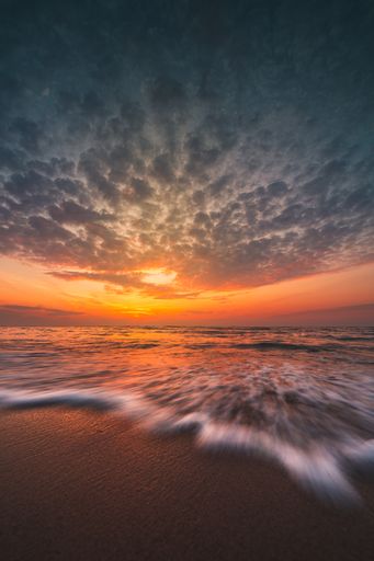 A beautiful long exposure shot of a beach with waves coming in under a bright sunset sky
