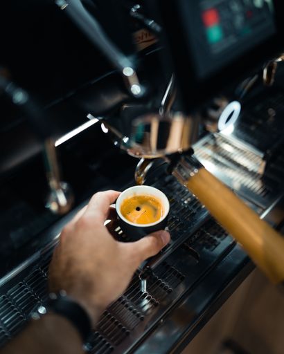 A vertical selective focus shot of a male hand picking up a cup of espresso from the coffee machine