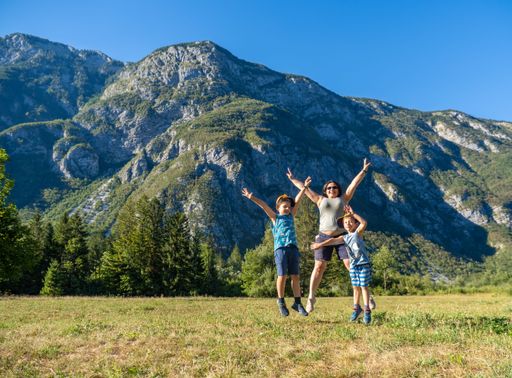 A Caucasian mother with sons happily jumping on green grass with a mountainous background