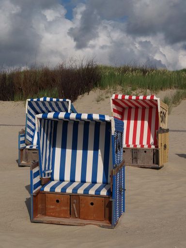 The colorful hooded beach chairs, on the sandy beach of Langeoog island in the North Sea, on a cloudy day, with green grass in the background