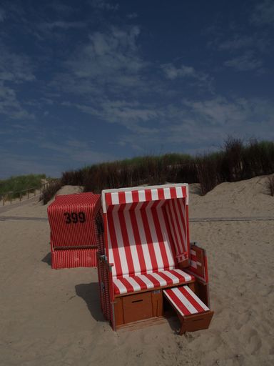 Striped hooded beach chairs, on the beach of Langeoog island in the North Sea, on a cloudy day, with a beach path, and green grass in the background