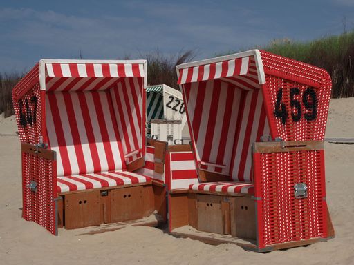 Red hooded beach chairs, on the beach of Langeoog island in the North Sea, on a cloudy day, with a beach path, and green grass in the background
