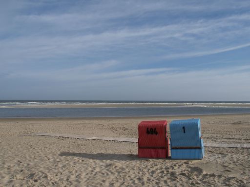 Colorful hooded beach chairs, on the sandy beach of Langeoog island in the North Sea, on a cloudy day with a sea view in the background