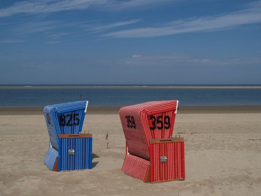 Red and blue hooded beach chairs, on the beach of Langeoog island, along a beach path, with a sea view