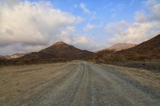 A road surrounded by hills covered in small rocks and sand under a blue cloudy sky