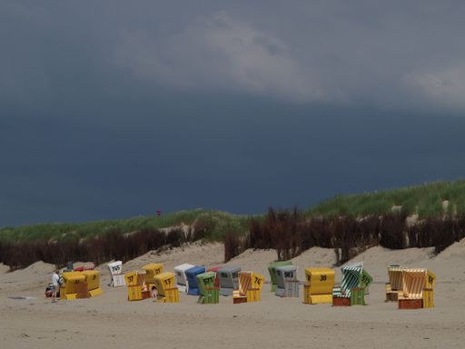 Colorful hooded beach chairs, on the beach of Langeoog island in the North Sea, on a cloudy day, and green grass in the background