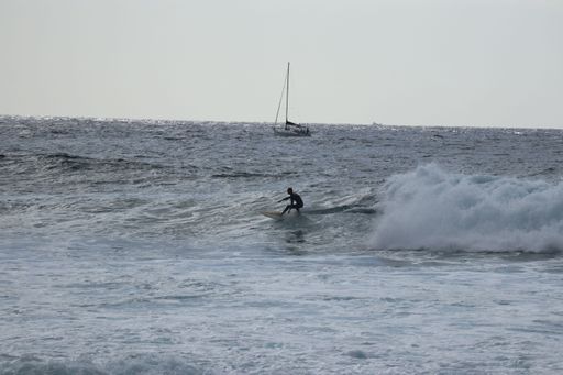 A scenic view of a person surfing on the waves in Tenerife with a beautiful seascape in the background