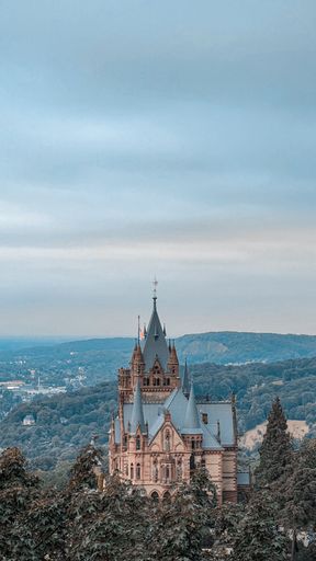 A vertical shot of Schloss Drachenburg in the middle of woods with a beautiful sky in the background