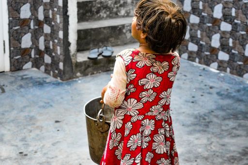 A beautiful child wearing a red dress holding a bucket shot from  behind with a blurred background