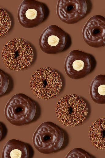 A vertical top shot of chocolate glazed donuts on the brown background