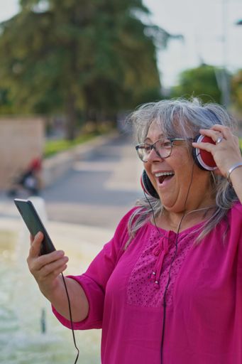 woman with white hair and glasses in a video call with her cell phone surprised smiling
