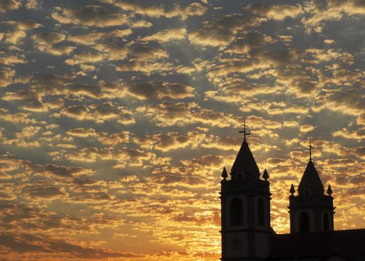 A scenic low angle shot of stratus clouds during sunrise with a silhouette of a church