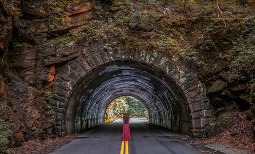 A female standing in front of a tunnel on the road with arms raised up, freedom concept