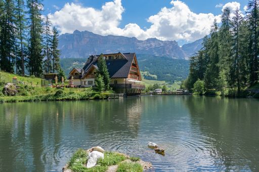 The beautiful Sompunt Lake with ducks swimming and a small house and mountains in the background in Alta Val Badia