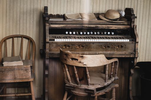 An old wooden piano with music sheets on top and chairs around