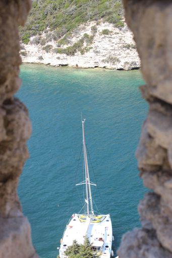 A small white boat which can be seen through an opening of a stone wall