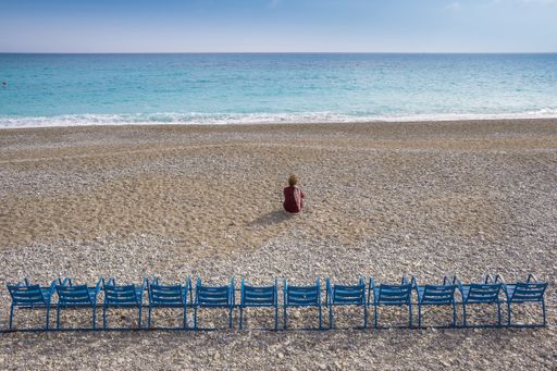 A person sitting on a beach shore looking at the sea waves with a blue sky in the background shot from behind