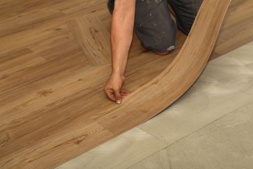 A worker installing new parquet vinyl tiles on floor