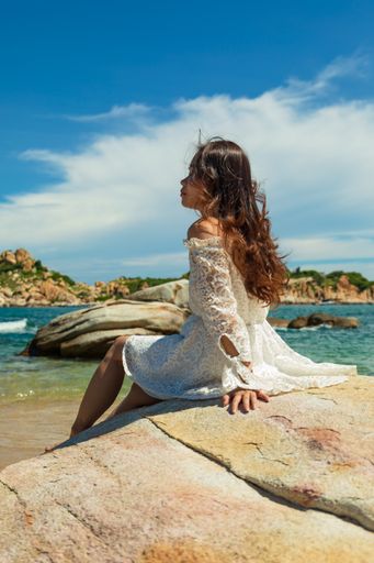 A vertical shot of a pretty Asian girl sitting on rocks near the beach