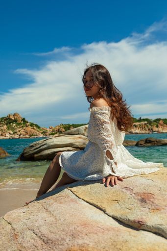 A vertical shot of a pretty Asian girl sitting on rocks near the beach