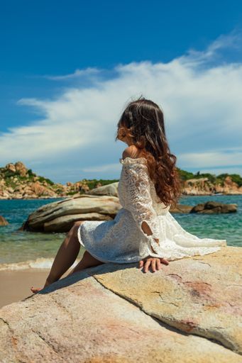 A vertical shot of a pretty Asian girl sitting on rocks near the beach