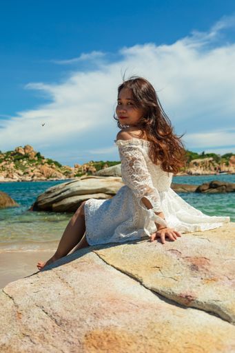 A vertical shot of a pretty Asian girl sitting on rocks near the beach