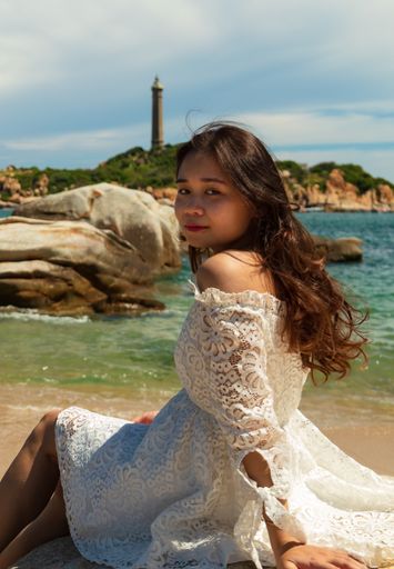 A vertical shot of a pretty Asian girl sitting on rocks near the beach